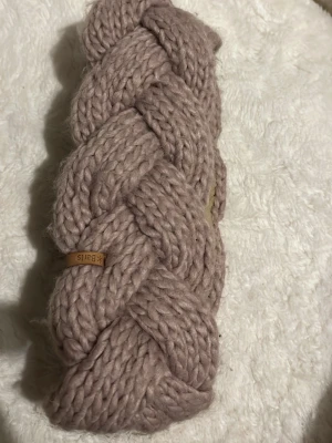 Beige flätad pannband från Barts - Säljer ett snyggt och chunky stickat pannband från Barts i beige färg. Pannbandet har en bred flätad design och är fodrat med mjukt fleecefoder på insidan för extra värme. Perfekt accessoar för kalla dagar och en trendig look.