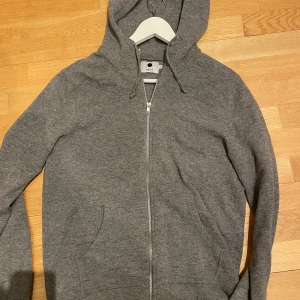 NN07 stickad hoodie i merinoull - Säljer en stilren grå hoodie från NN07 i 100% merinoull med dragkedja och fickor framtill.   Aldrig använd men passade tyvärr inte mig Nypris 2200kr men jag säljer den för bara 550 kr. Pris kan diskuteras snabb affär
