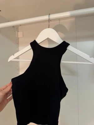 Svart ribbad linnetopp från H&M Divided - Svart ribbad linnetopp från H&M Divided. Toppen är ärmlös med hög halsringning och croppad passform, perfekt till jeans eller kjol. Tillverkad i mjuk bomullsmix som sitter skönt mot kroppen.🤎