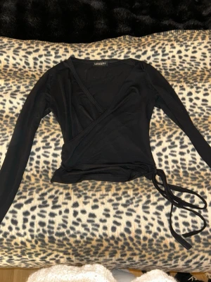 Svart omlottopp från Missay - Säljer en svart omlottopp från Missay med långa ärmar och knyt i sidan. Toppen har en djup v-ringning och sitter tight på kroppen. Använd ett fåtal gånger ca 3 gånger. Inga fläckar. 