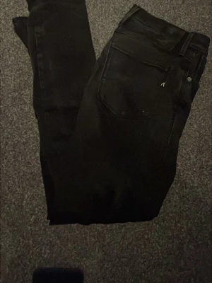 Svarta Replay jeans med raka ben - Svarta jeans från Replay med klassisk femficksdesign och diskret logga på bakfickan. Jeansen har raka ben och är tillverkade i ett mjukt denimtyg som sitter snyggt. Perfekta för dig som gillar stilrena och enkla jeans.priset inte hugget i sten