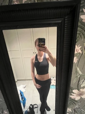 Svart sport-bh från NA - Säljer en svart sport-bh från NA med brottarrygg och vit logga framtill. Bh:n har breda axelband och ger bra stöd, perfekt för träning och gym. Materialet är stretchigt och följsamt för maximal komfort.