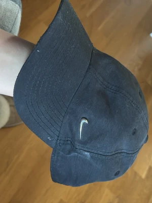 Svart Nike keps med metallogo - Snygg svart keps från Nike med den klassiska metallfärgade swoosh-loggan framtill. Justerbart spänne baktill för perfekt passform. Tillverkad i mjukt bomullstyg och har böjd skärm för en avslappnad look.