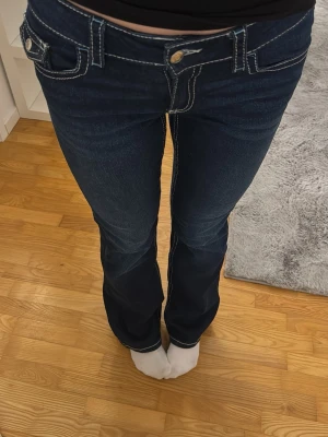 Mörkblå bootcut jeans från Gina - Säljer ett par mörkblå bootcut jeans med vita kontrastsömmar och klassisk femficksdesign. Jeansen har låg midja och är tillverkade i ett stretchigt denimtyg som sitter snyggt över höfterna och låren innan de släpper ut vid bensluten. Storlek 170 vilket motsvarar S!💗dom är använda 2 gånger och känns som nya! hör gärna av er vid frågor💗