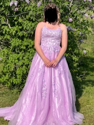 Ljuslila balklänning 💕 - Romantisk ljuslila långklänning med tunna axelband och vackra spetsdetaljer på livet. Kjolen är voluminös med flera lager tyg och broderade blommor. Perfekt för balen 💕