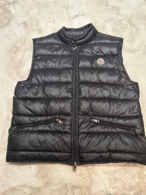 Svart dunväst  - Snygg svart dunväst  med quiltad design och hög krage. Västen har två dragkedjefickor Perfekt för lager-på-lager och håller dig varm med stil.