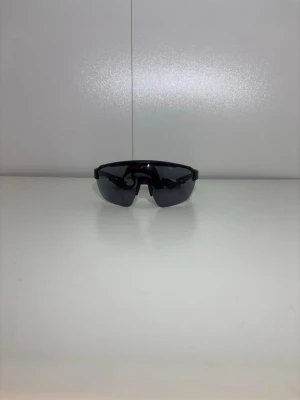  Innebandy glasögon  - Säljer ett par sportiga solglasögon med svart båge och spegeltonade linser. Glasögonen har en omslutande form som passar perfekt för utomhusaktiviteter och ger ett coolt, futuristiskt intryck. Materialet är lätt plast och designen är aerodynamisk.