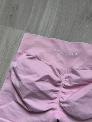 Ljusrosa seamless shorts från Relode - Säljer ett par ljusrosa seamless shorts från Relode. De har hög midja, scrunch-detalj bak och är tillverkade i ett stretchigt material som passar perfekt för träning. Shortsen har en tight passform och är designade för att framhäva formerna. Shortsen är aldrig använda utan köpta för bara några veckor sedan, storlek M. Nypris är 579kr