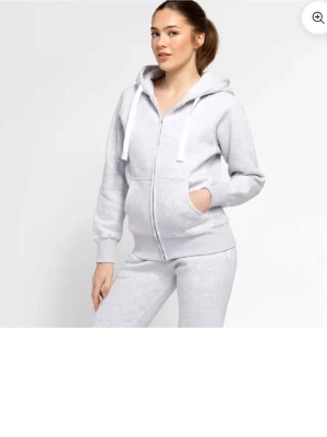 Ljusgrå hoodie från russemerch  - Snygg ljusgrå hoodie från russemerch med dragkedja. Hoodien har huva med breda vita snören och ribbade muddar vid ärmslut och nederkant. Jätteskönt material och sparsamt använd. I storlek M. 