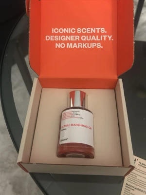 Floral Marshmallow parfym från Dossier - Floral Marshmallow är en parfym från Dossier med en stilren, genomskinlig glasflaska och silverfärgad kork. Doften har noter av marshmallow, neroli, bergamott, apelsinblomma, kaprifol, jasmin, ambra, vanilj och mysk. Flaskan har en minimalistisk vit etikett med röd text.