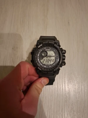 Svart digital sportklocka - Digital sportklocka i svart med robust design och flera knappar runt urtavlan. Klockan har digital display, gummiband och funktioner som datum, alarm, lysande läge och stoppur. Vattentålig upp till 30 meter. Perfekt för dig som gillar en sportig och praktisk stil. Priset är självklart diskuterbart