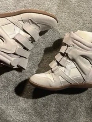 Isabel Marant vita sneakers med kardborre - Säljer ett par vita sneakers från Isabel Marant med chunky design och flera kardborreband. Skorna har en mix av mocka och läder, samt en beige gummisula. Perfekta för dig som gillar streetstyle och vill ha något unikt till din outfit.