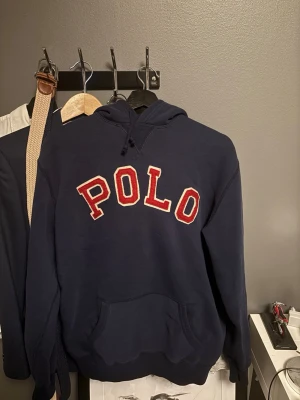Mörkblå hoodie från Polo Ralph Lauren - Mörkblå hoodie från Polo Ralph Lauren med stor röd och vit POLO-text på bröstet. Storlek S men sitter som en M