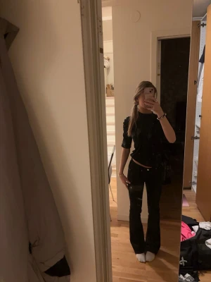 Svart topp med puffärm - En svart topp med puffade axlar och halvlånga ärmar. Toppen har en hög halsringning och är figurnära i modellen. Perfekt att styla med både jeans och kjol.