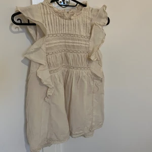 Beige blus med volangdetaljer - Söt beige blus med volanger längs axlarna och spetsdetaljer framtill. Blusen är ärmlös och har rundad hals med veckade partier på bröstet. Perfekt för dig som gillar romantisk och luftig stil. Priset kan diskuteras !!