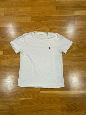 Vit t-shirt från Ralph Lauren - Klassisk vit t-shirt från Ralph Lauren med rund halsringning och korta ärmar. T-shirten har en liten broderad logga i svart på bröstet. Perfekt basplagg i mjuk bomull.