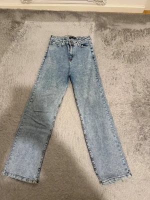 Ljusblå raka jeans i klassisk modell - Säljer ett par ljusblå jeans med rak passform och hög midja. Jeansen har fem fickor, bälteshällor och stängs med dragkedja och knapp. Perfekta för dig som gillar en enkel och tidlös look.