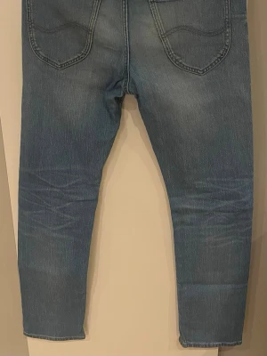 Blå Lee jeans med raka ben - Säljer ett par klassiska blå jeans från Lee med raka ben och snyggt slitna detaljer. Jeansen har två bakfickor och en Lee-lapp i läder bak i midjan. Perfekta för dig som gillar tidlös denimstil. Hör av er vid minsta fråga 😋😋