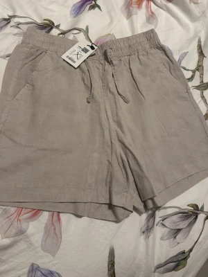 Beige linneshorts med snörning från Lager 157  - Snygga beige shorts i linne från Lager 157 med elastisk midja och snörning. Perfekta för varma dagar och har praktiska sidofickor. Lätta att matcha med olika toppar för en chill look. Linne material, kostade 80kr helt oanvända 