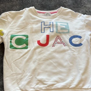 Vit tröja från Marc Jacobs - Säljer en cool vit tröja från The Marc Jacobs med färgglada bokstäver och detaljer i olika färger. Tröjan har långa ärmar och en rund halsringning med rosa kant. Perfekt för en färgglad stil!