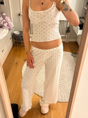 Vit pyjamas med blå blommor - Söt pyjamas i två delar med vitt ribbat tyg och små blå blommor. Linnet har smala axelband och volangkant, byxorna är vida och mjuka. Perfekt för mysiga hemmakvällar. Settet är ifrån Lindex och är i storlek S i både linnet och byxorna. Har inga defekter och är ett väldigt skönt/tunt tyg som får de jätteskönt å sova i 