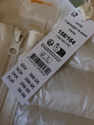 Vit dunjacka från Gina Tricot - Snygg cremevit dunjacka från Gina Tricot med quiltad design och ribbade detaljer vid ärmslut och nederkant. Jackan har dragkedja framtill och praktiska fickor. Perfekt för kyliga dagar och enkel att matcha med olika outfits.