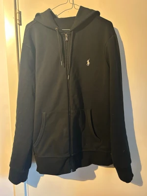 Svart zip hoodie från Polo Ralph Lauren - Säljer min svarta Ralph lauren hoodie för jag inte använder den så mycket skicket är 8,5/10 och den passar L. Dem vita prickarna är bara lite ull som kommit av från jackan och tvättas bort innan jag skickar den till dens nya ägare såklart!
