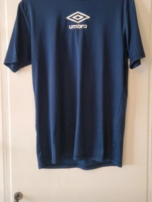 Sportset - Ett blått träningsset från Umbro med t-shirt och shorts Setet är gjort i polyester och har Umbro-loggan i vitt på både tröjan och shortsen. Storlek L på båda. Mkt fint skick. 