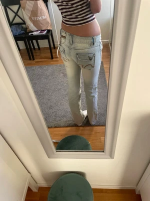 Replay ljusblå jeans med fickdetaljer - Säljer ett par ljusblå Replay jeans med snygga fickor bak och fram, dekorerade med bruna sömmar och coola knappar. Jeansen har dragkedja och raka ben med normal passform. Perfekt för dig som gillar street och detaljerad design. Midja 35,5 cm längd 84 cm