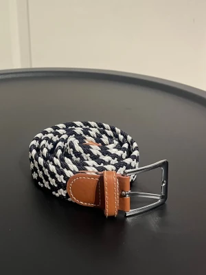 Flätat bälte 105 cm  - Flätat bälte i färgerna svart och vitt. Det är 105 cm långt, men materialet är stretchigt. Aldrig blivit använt.