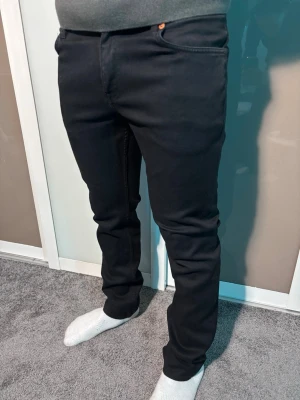 Svarta jeans från BOSS - Säljer ett par svarta jeans från BOSS med klassisk femficksdesign och diskreta oranga detaljer. Byxorna har rak passform och normal midja, tillverkade i mjuk bomullsblandning för skön känsla. Perfekta till både hoodie och skjorta.