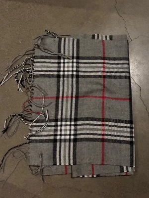 Grå rutig halsduk med fransar - Säljer en grå halsduk med klassiskt rutigt mönster i svart, vitt och rött. Halsduken har fransar i ändarna och är tillverkad i ett mjukt tyg som känns skönt mot huden. Perfekt att svepa runt halsen för en snygg look. Lik en sådan från Burberry💥💥💥💥