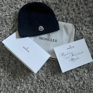 kabelstickad mössa från Moncler - Snygg mörkblå stickad mössa från Moncler med klassisk Moncler-logga framtill. Mössan har en ribbad kant och är tillverkad i ett mjukt och värmande material, perfekt för kyliga dagar och är givetvis äkta och tags finns men är inte med på bilden. pris kan diskuteras 👌