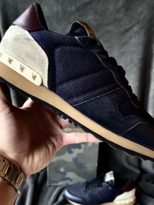 Valentino Garavani Rockrunner sneakers - Snygga Valentino Garavani Rockrunner sneakers i mörkblå mesh och mocka med beige och vinröda detaljer. Skorna har en platt sula i beige och ikoniska pyramidnitar på hälen. Klassisk snörning och rund tå. Perfekt för dig som vill ha en lyxig och unik sneaker.