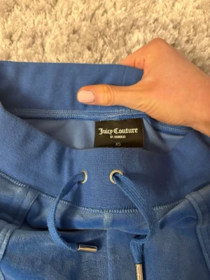  Blå Juicy Couture byxor  - Säljer ett par blå mjukisbyxor från Juicy Couture i storlek XS. Dem är använda sparsamt och är i fint skick. Kan såklart sänka priset vid snabbt köp. Skriv till mig om ni har frågor. Obs. Byxorna har tidigare vart uppsydda men materialet är inte skadat (se bilder) 