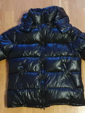 Svart Moncler pufferjacka med huva - Säljer en svart pufferjacka från Moncler i storlek M. Jackan har en glansig finish, huva, dragkedja framtill och två snedställda fickor med dragkedja. Moncler-logga på ärmen och quiltad design som ger en cool look. Perfekt för kalla dagar.
