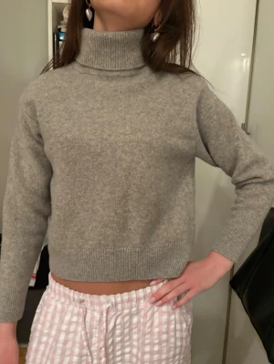 Grå polotröja i ull, croppad - Snygg grå polotröja med croppad passform och ribbade muddar. Tröjan har hög polokrage och är stickad i mjuk ull, perfekt för kyliga dagar. Enkel och stilren design som funkar till många olika outfits.