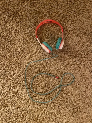 ZAGG kabelanslutna hörlurar med nyckelpigemotiv - Färgglada kabelanslutna hörlurar från ZAGG med bekväma turkosa öronkuddar och nyckelpigemotiv på sidan. Passar barn och unga, har justerbar bygel och 3,5 mm kontakt. Ser ut att vara i gott skick utan synligt slitage.