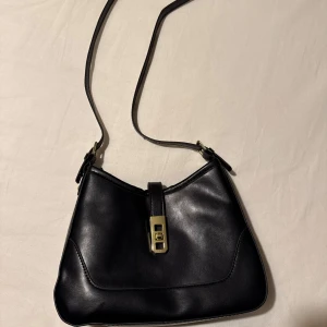 Svart axelväska med gulddetalj - Säljer denna svarta axelväska i skinn med justerbar rem (kommer också med en mindre som ligger i väskan). Helt oanvänd & så fin!💕