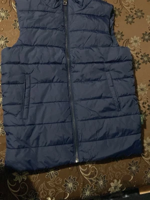 Mörkblå dunväst från Indicode - Säljer en mörkblå dunväst från Indicode i storlek small. Västen har quiltad design, två sidofickor och dragkedja framtill. Perfekt för lager-på-lager och chill stil. Materialet är syntet , vilket gör den lätt och smidig att bära. Priset ej hugget i sten⛱️ storlek S