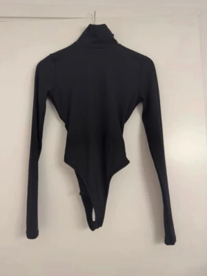 Svart polotopp body med öppen rygg och knyt - Säljer en svart långärmad polo body  i stretchigt material med öppen rygg och snygg knytning bak. Bodyn är tight och perfekt att styla med höga jeans. Enkel men ändå unik detalj med öppen rygg. 