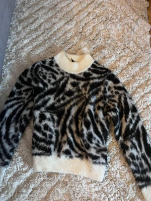 Zebramönstrad stickad  - SÄLJS INTE LÄNGRE! Säljer en fluffig och mysig stickad polotröja med zebramönster i svart och vit. Tröjan har ribbade muddar vid hals, ärmslut och nederkant. Perfekt för dig som vill sticka ut med en cool look under höst och vinter.