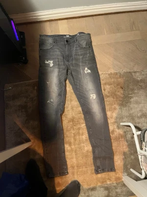 Grå jeans med slitningar - Ett par grå jeans med snygga slitningar. Storlek 33/34, skulle säga att de passar bra för 32/33. Okänt märke.