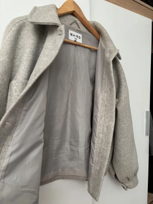 Beige overshirt från NA-KD i ullmix - Snygg beige overshirt från NA-KD med stora bröstfickor, knappar framtill och klassisk krage. Jackan är i ullmix och har en loose passform med långa ärmar och knappdetalj vid ärmslut. Perfekt lager-på-lager-plagg för kyligare dagar.