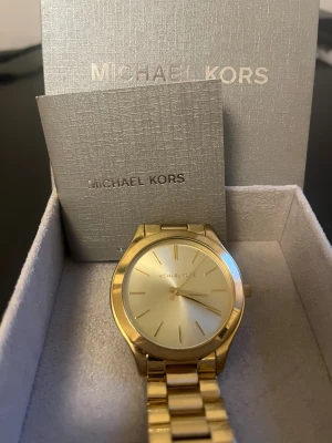 Klocka från Michael Kors modell Slim Runaway MK 3179 - Stilren guldig armbandsklocka från Michael Kors med metallänk och minimalistisk urtavla utan siffror. Klockan har en rund form och levereras i originalask med tillhörande manual. Perfekt accessoar för dig som gillar en clean och lyxig look.