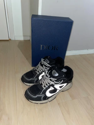 Svarta DlOR b30s - Säljer ett par svarta DlOR sneakers med feta reflekterande detaljer på sidorna. Skorna har chunky sula och coola kontraster mellan svart mesh och silvriga inslag. Perfekta för dig som vill sticka ut med lyxig streetstyle.