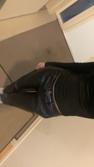 Svarta byxor med smal passform - Säljer ett par svarta skinnbyxor med smal passform och klassiska fickor fram. Byxorna har midja med knapp och dragkedja, samt en snygg glansig finish som ger en cool look. Perfekta för dig som vill sticka ut lite extra.