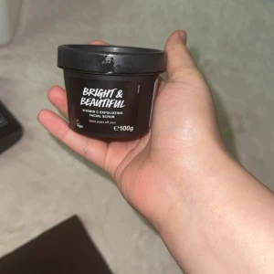 Bright & Beautiful Vitamin C Facial Scrub - Bright & Beautiful Vitamin C Exfoliating Facial Scrub från Lush i en svart rund plastburk, 100g. Skrubben har en mörklila färg med rosa inslag och innehåller bland annat grapefrukt, kol och vitamin C för en fräsch och strålande hud.