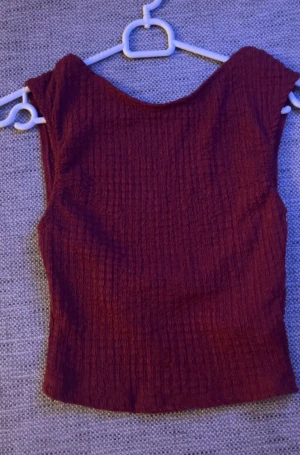 Vinröd croppad topp med struktur - Säljer en vinröd croppad topp med snyggt strukturerat tyg och bred halsringning. Toppen är ärmlös och har en tight passform som framhäver siluetten. Perfekt att styla med jeans eller kjol. Öppen i ryggen