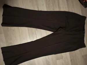 Bruna kostymbyxor från ASOS Design - Snygga bruna kostymbyxor från ASOS Design med klassisk rak passform och hög midja. Byxorna har en stilren look med vida ben och är tillverkade i ett mjukt material som ger en skön känsla. Perfekta för dig som gillar en clean och dressad stil.